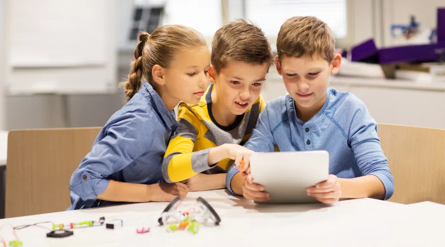 Group of three kids talking over a tablet while they build robotics equipment in an afterschool program.