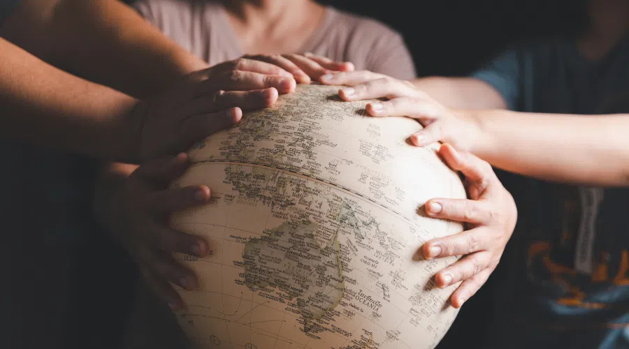 A globe with a couple sets of hands on it looking where to travel on their next mission trip.