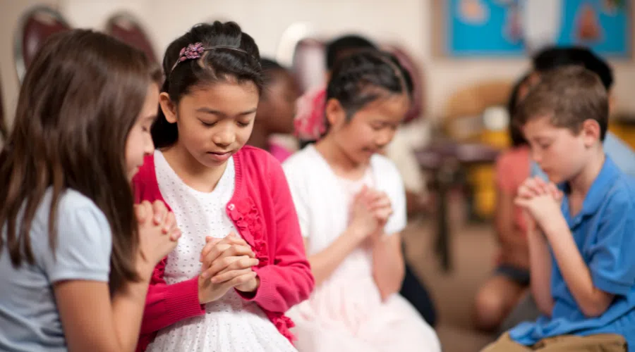 group of four children bowing their heads, locking their hands, and praying in while on a mission trip.