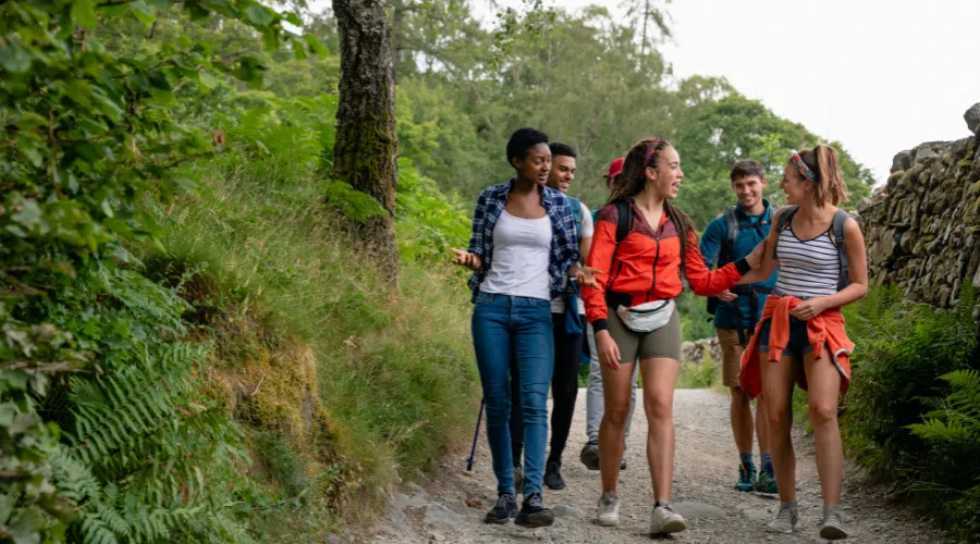 group of young adults hiking and talking to each other in a friendly way. they are on a path with vegetation around them while on a mission trip
