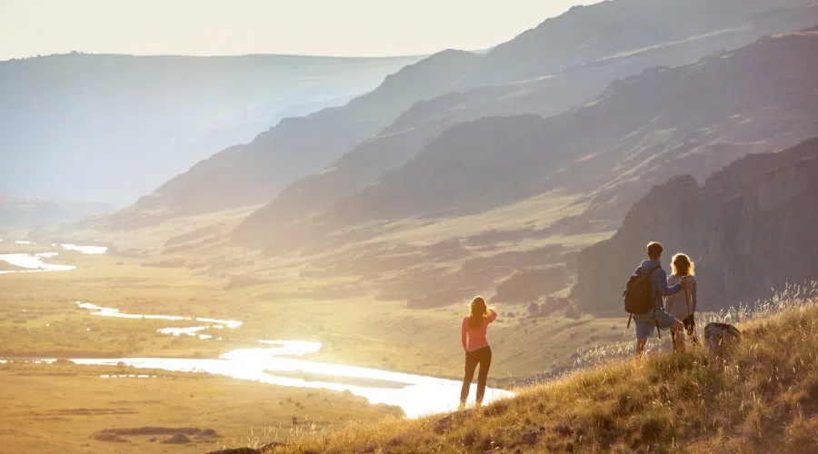 group of three people hiking in mountains at sunset pictured from a distance. They are overlooking a stream
