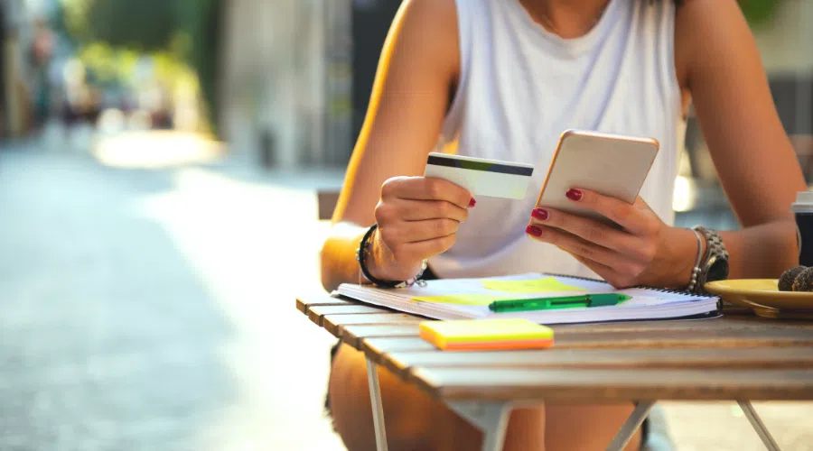 women using a credit card to pay on her phone. She is typing in her payment information into the digital payment processor while sitting at a table outside.