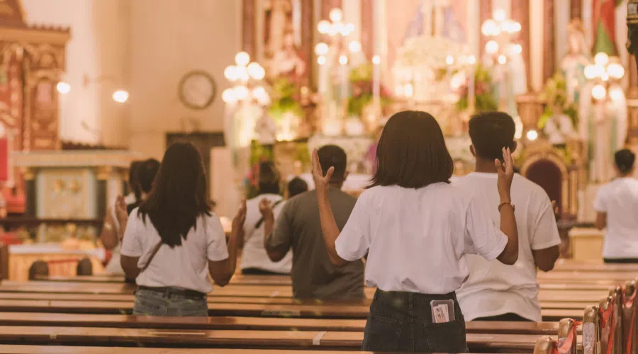 Perspective of standing in the back of the church where people are standing and praying looking at the alter.