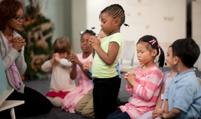A group. of young kids praying a youth group setting.