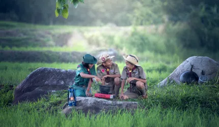 Three boy scouts gathered around a log in the forest