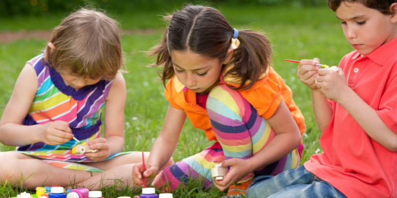 three kids painting on paper in the grass
