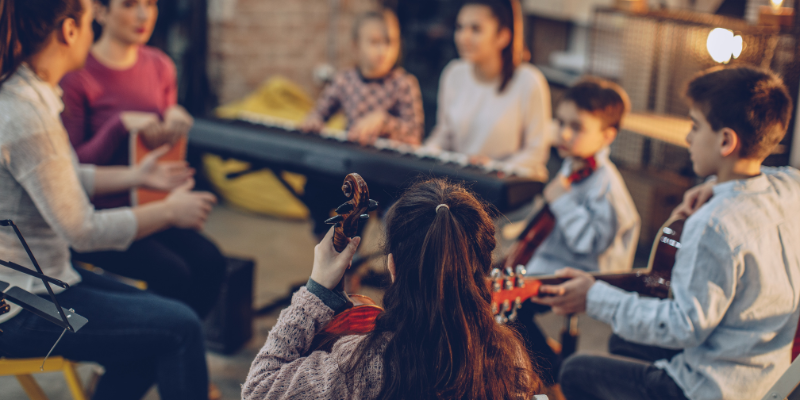 a circle of teenagers playing the cello, the piano, and guitar.