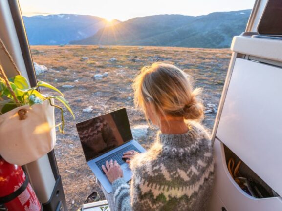 Blonde woman siting in an open van on her laptop
