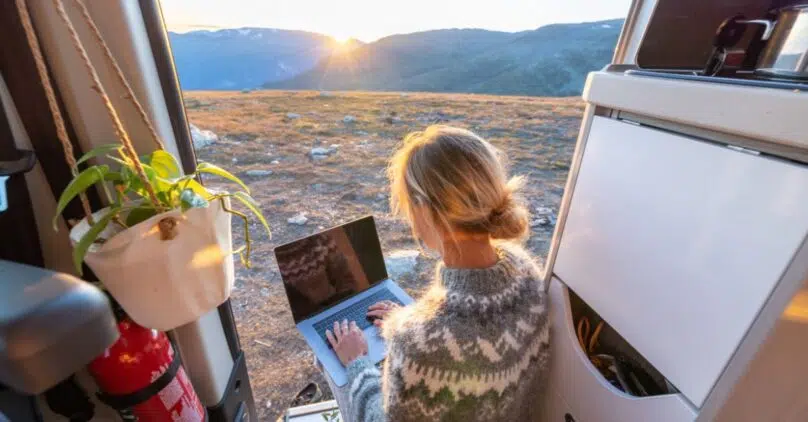 Blonde woman siting in an open van on her laptop
