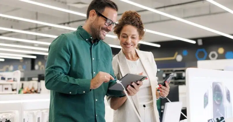 Two co-workers look at a tablet together smiling