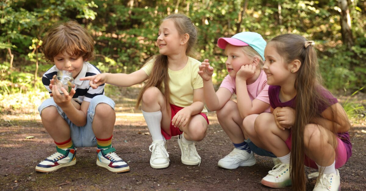 4 young girls kneeling and looking at a jar of marbles outside in the forest